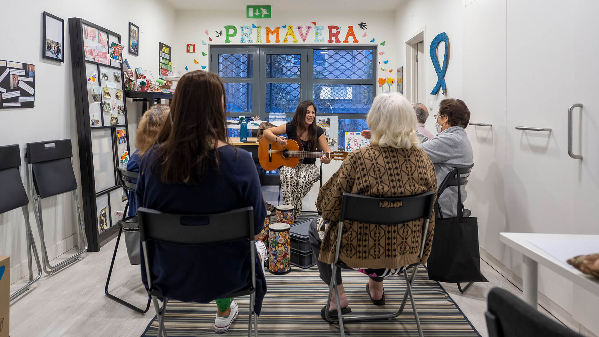 Senhora toca guitarra em confraternização com grupo de idosos na sala da ANADIC